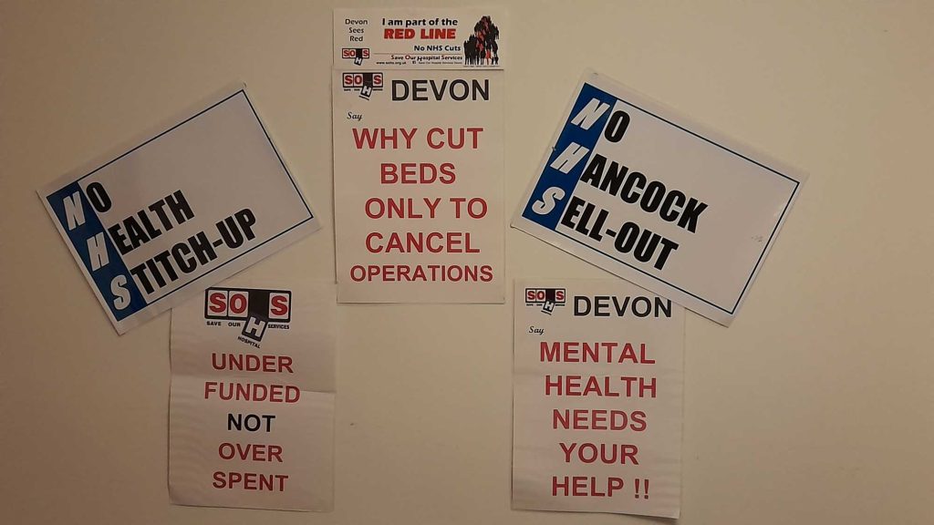 A group of posters on a wall. They say: 'No Health Stitch-up'. Under funded not over spent', 'Why cut beds only to cancel operations', 'No Hancock Sell-out' and 'Mental Health needs your help!' 